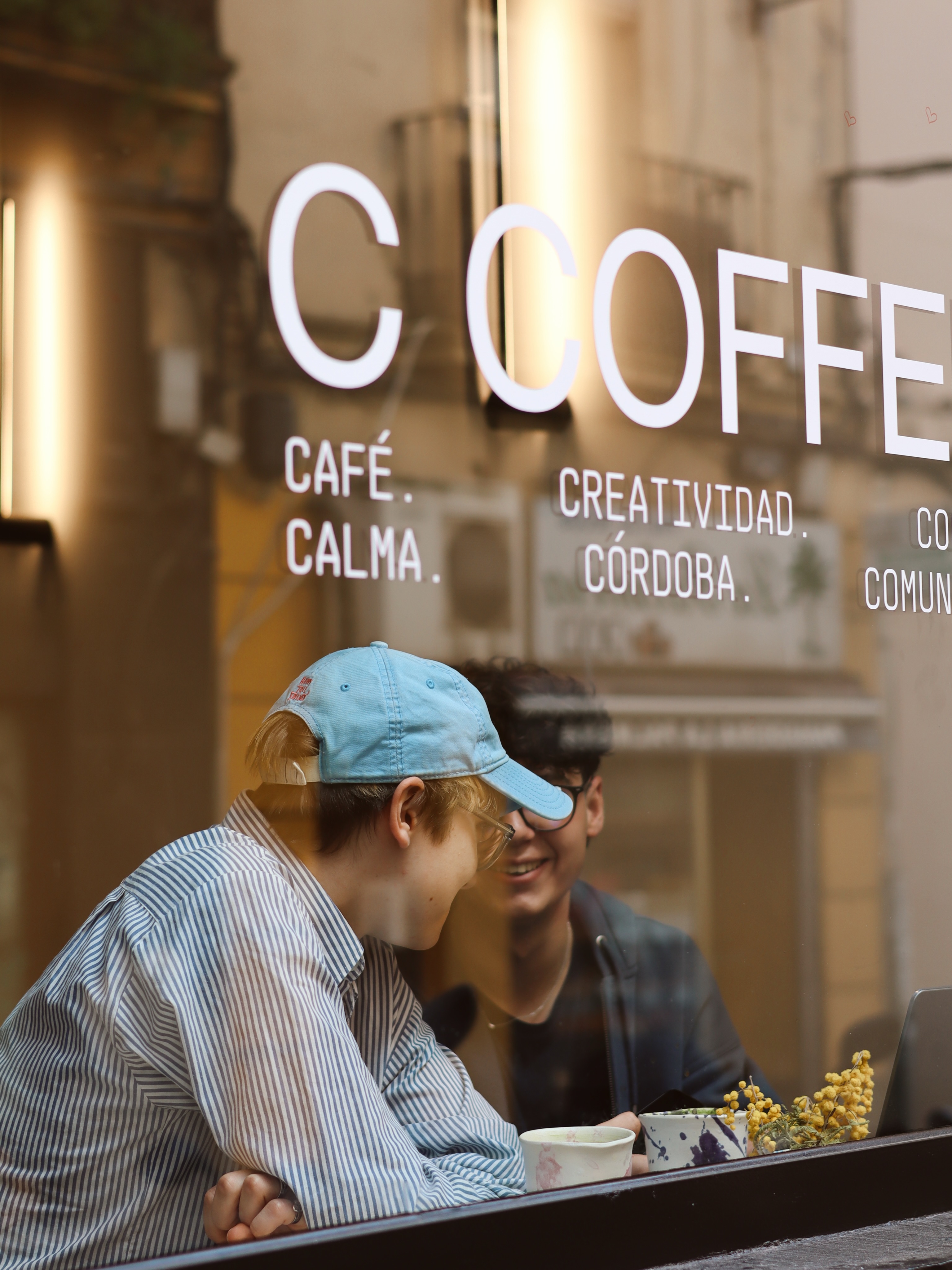 Dos clientes conversando tras el escaparate de C Coffee con el logotipo y los valores de la marca