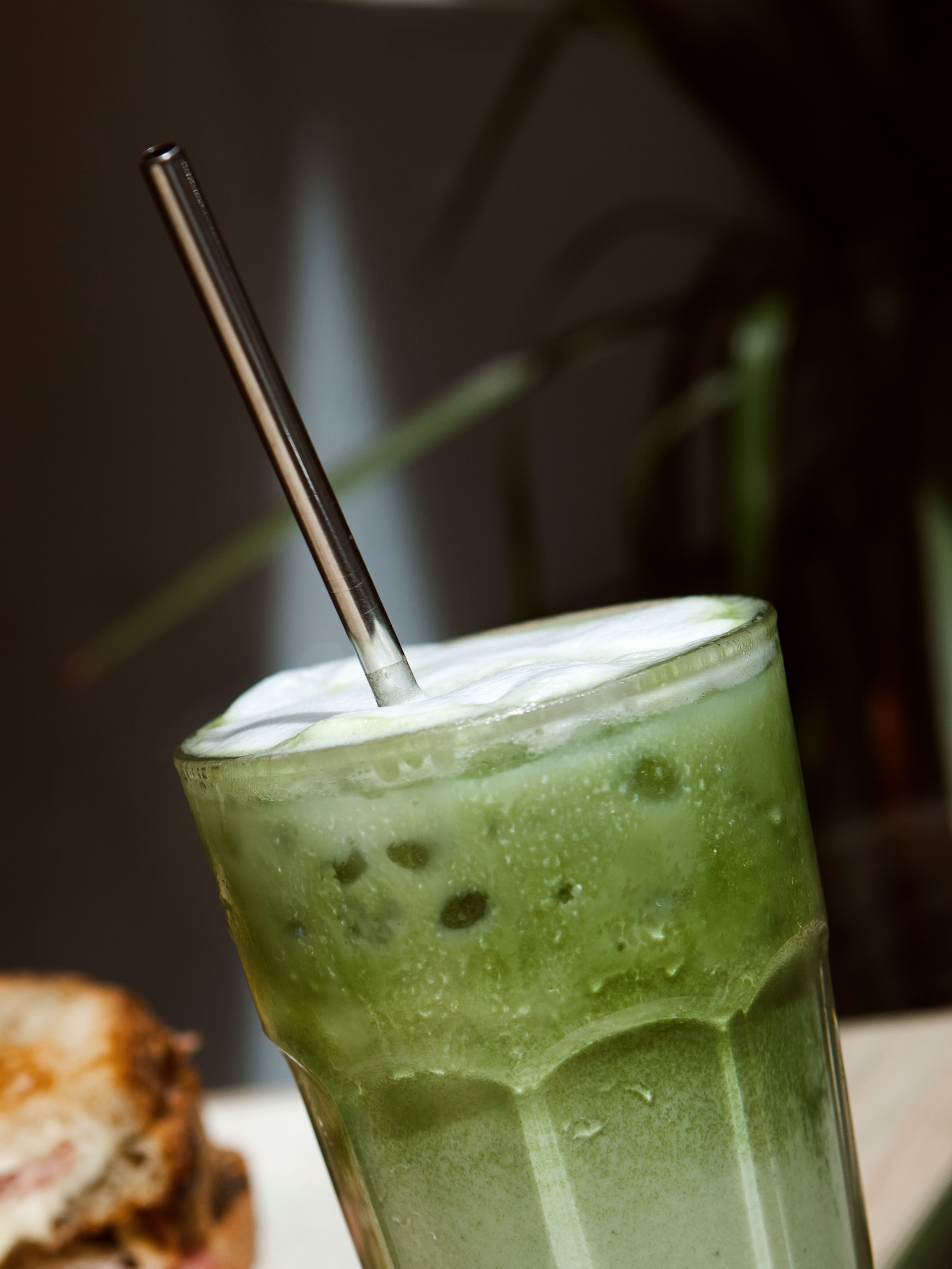 Matcha latte helado servido en un vaso alto con pajita metálica