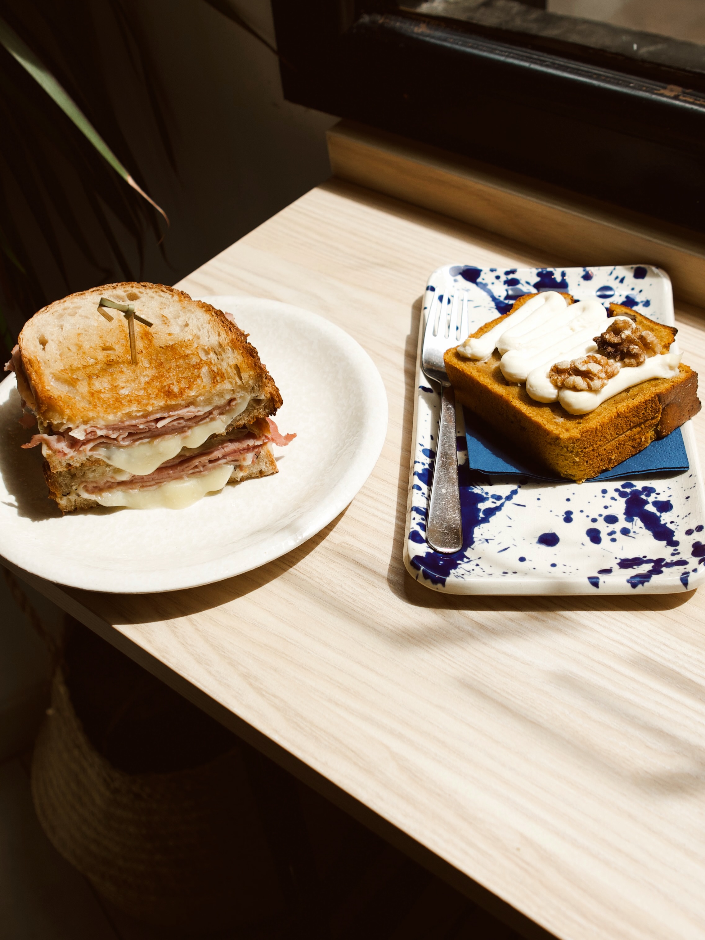 Sándwich mixto y una porción de carrot cake con nueces sobre una mesa de madera al sol